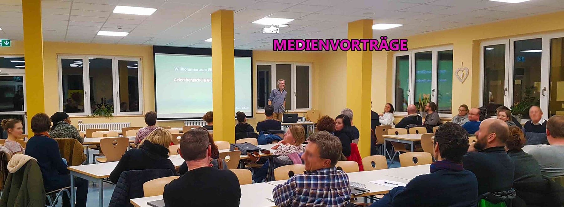 Publikum an Tischen in einem Saal bei einem Medienvortrag